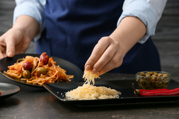 Woman preparing tasty Pasta Puttanesca at table in kitchen, closeup