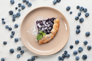 Plate with piece of tasty blueberry galette on light background