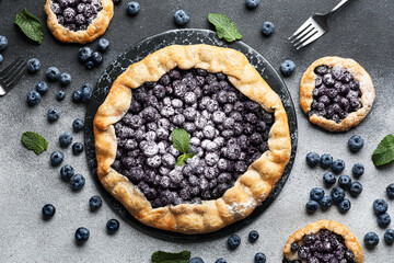 Plate with tasty blueberry galettes on dark background