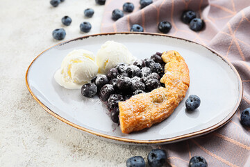 Plate with tasty blueberry galette and ice cream on light background, closeup