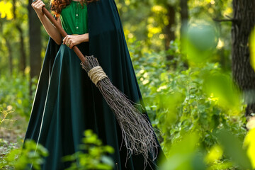 Young witch with broom in green forest