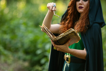 Young witch with spell book in green forest