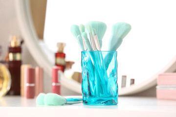 Glass with set of stylish makeup brushes on light table