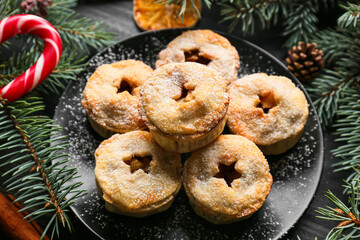 Plate with tasty mince pies and Christmas decor on dark background
