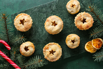 Board with tasty mince pies and Christmas decor on green background