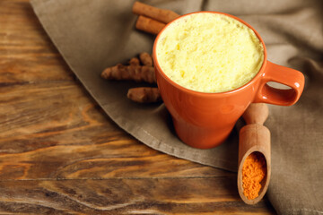 Cup of tasty latte and scoop with turmeric powder on wooden background