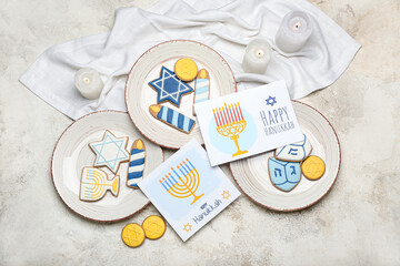 Plates with cookies and greeting cards for Hanukkah celebration on grunge background