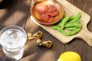 グラスに注がれた冷たく冷えたハイボールとサラミと枝豆のおつまみ