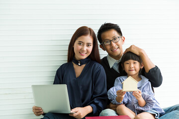 Portrait of young Asian family sitting together at home. Young Asian father, mother and their cute little daughter sitting together and looking at camera with happy and smile at home in holiday