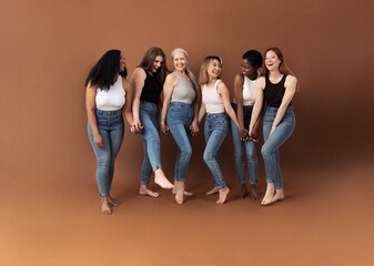 Obraz premium Six happy women in casuals standing together in studio against brown background