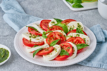 Arranged italian caprese salad in restaurant. Fresh mozarella, sliced tomatoes, basil leaf, olive oil. Organic and healthy. Homemade crushed pesto sauce. Traditional recipe. Mediterranean cuisine