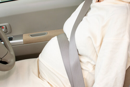 A young pregnant Asian woman wears a seatbelt inappropriately