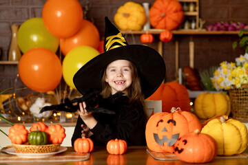 halloween, a baby girl in a witch costume with pumpkins and a big spider in a dark kitchen scares at the Halloween party, smiling, rejoicing and fooling around