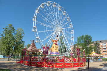 Carousel and Ferris wheel in the children's city amusement park on a sunny July morning. Velikiye Luki - obrazy, fototapety, plakaty