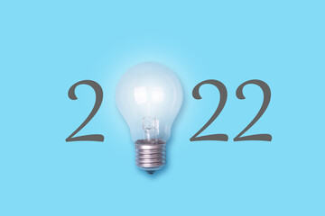 2022, and a glowing light bulb, on a blue background. Concept of new ideas for the new year.
