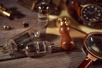 Steampunk still life - old vintage objects on a wooden background. Leather wrist watch, dark glasses, old tube lamps, magnifying glass, gears
