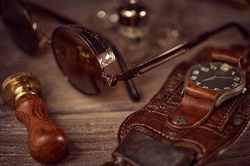 Steampunk still life - old vintage objects on a wooden background. Leather wrist watch, dark glasses, old tube lamps, magnifying glass, gears