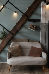 Modern Scandinavian hygge styled home living room interior design. Comfortable cozy sofa, with pillows, glowing garland lights, stairs, blue wall. Elegant Christmas, New Year celebration decorations © Floral Deco
