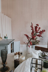 Christmas dinner serving. Bright dinning room interior with dusty pink walls, table, red berries bouquet, decorations. Christmas celebration evening