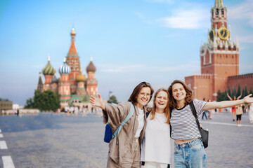 Three young women students friends happily walking travelling along Red Square in Moscow