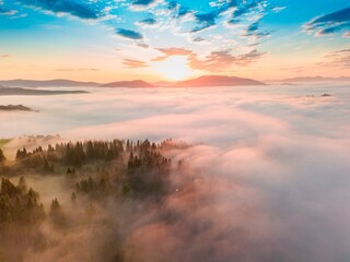 Fog spreads over the mountains at dawn. The sun rises on the horizon. Ukrainian Carpathians in the morning. Aerial drone view.