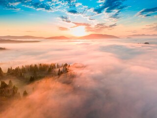 Fog spreads over the mountains at dawn. The sun rises on the horizon. Ukrainian Carpathians in the morning. Aerial drone view.