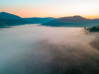 Fog spreads over the mountains at dawn. The sun rises on the horizon. Ukrainian Carpathians in the morning. Aerial drone view.