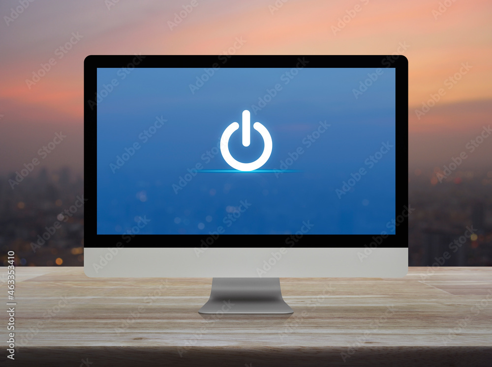 Poster power button icon on desktop modern computer monitor screen on wooden table over blur of cityscape o