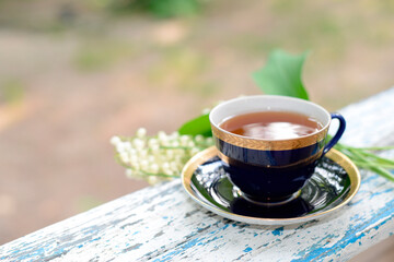 Tea and bouquet of lily-of-the-valley flowers on the garden. Cup of black or herbal tea. Hot, beverage, Aromatic and healthy morning or afternoon tea in the open air. 