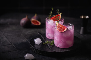 Purple fig cocktail with ice and thyme on dark background