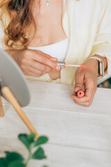 Young woman does makeup in front of a mirror at home and tests lipsticks on her hand, hands close-up.Self-care at home.Beauty concept.Selective focus,copy space.
