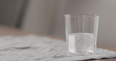 clear ice cube in tumbler glass on table