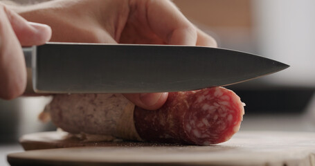 man slicing salami on olive board