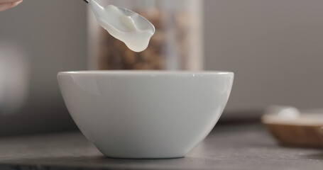pour white yogurt into white bowl on terrazzo countertop