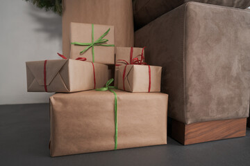 presents in paper wrap with ribbons under christmas tree indoor near couch with warm light