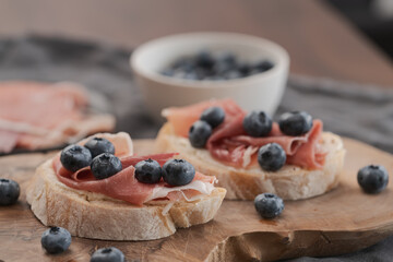 Bruschetta with prosciutto with cream cheese and blueberries on olive wood board