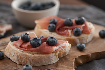 Bruschetta with prosciutto with cream cheese and blueberries on olive wood board