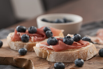 Bruschetta with prosciutto with cream cheese and blueberries on olive wood board