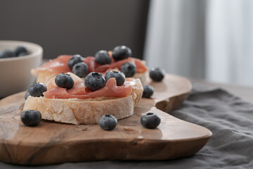 Bruschetta with prosciutto with cream cheese and blueberries on olive wood board
