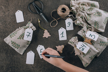 Preparation of christmas advent calendar. Presents wrapped in fabric eco bags. Flat lay, top view.