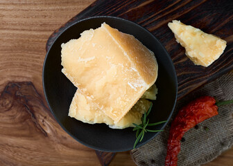 Layout of hard cheese on a dark background with spices. Pieces of parmesan cheese in a black plate.