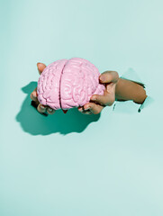 Woman's hands holding human brain thru the wall on vibrant green background. Creative idea or...