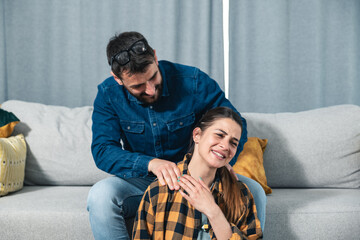 Young couple in love a girl sitting on the floor and a guy on the couch and gently massages her neck muscle to relax her muscles after a hard day and to relieve her of stress, couple home massage 