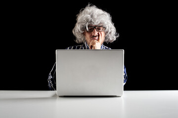 An elder serious man lost in thoughts in front of a laptop computer,