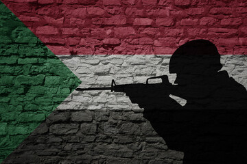 Soldier silhouette on the old brick wall with flag of sudan country. - obrazy, fototapety, plakaty