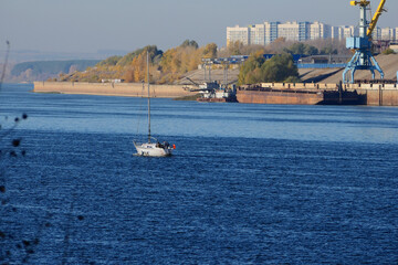 The sailboat goes along the river along the city and the construction site on the river bank.