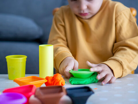 Toddler boy playing with modeling dough or plastelin with concentration and focus. Kid playtime with plasticine and shapes molds. Creativity and cognitive development toys for children.