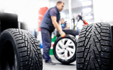 Naklejka na ściany i meble Concept car service replacement of winter and summer tires. Mechanic holding wheels at garage