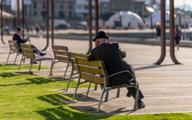 Hombre adulto irreconocible sentado en un banco frente al muelle en una mañana soleada - obrazy, fototapety, plakaty
