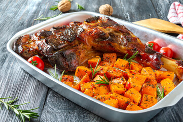 Roasted turkey leg and pumpkin pieces with aromatic herbs. Thanksgiving dish.
